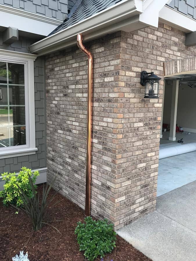 Copper downspout paired with a white K-style gutter on a home exterior