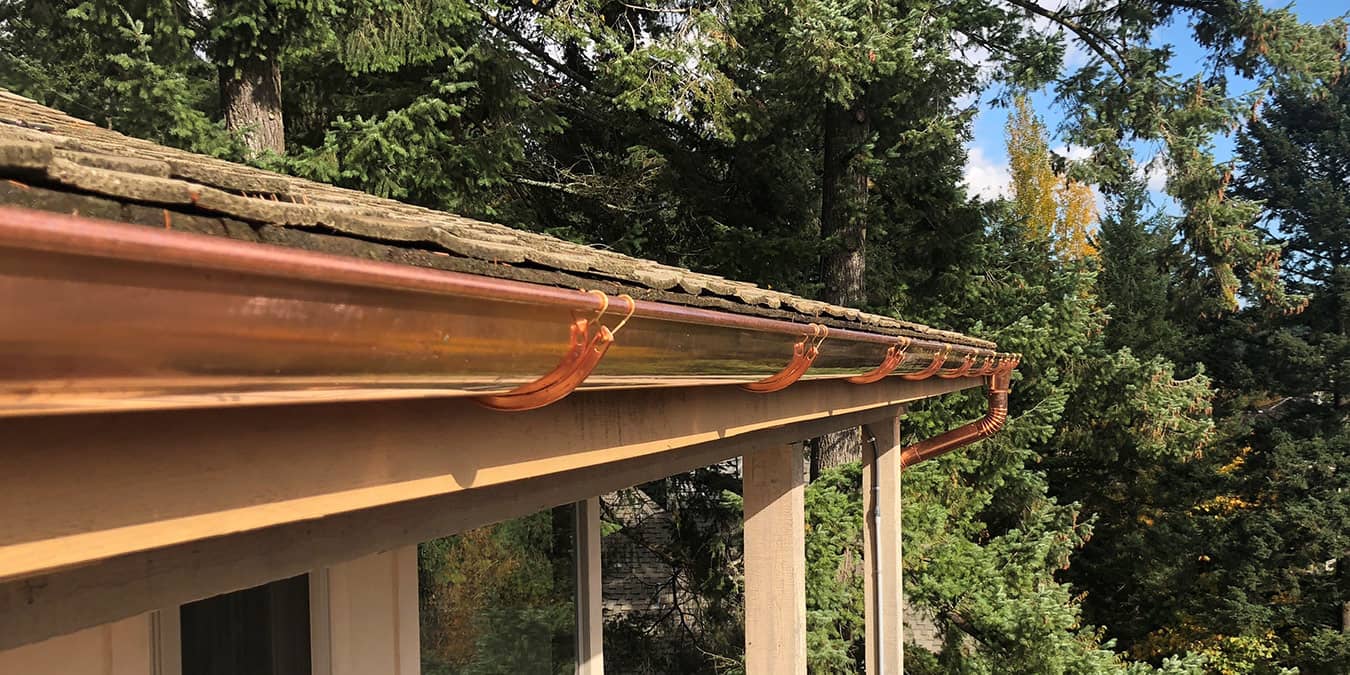 Copper half-round gutter installed under a shingle roof edge