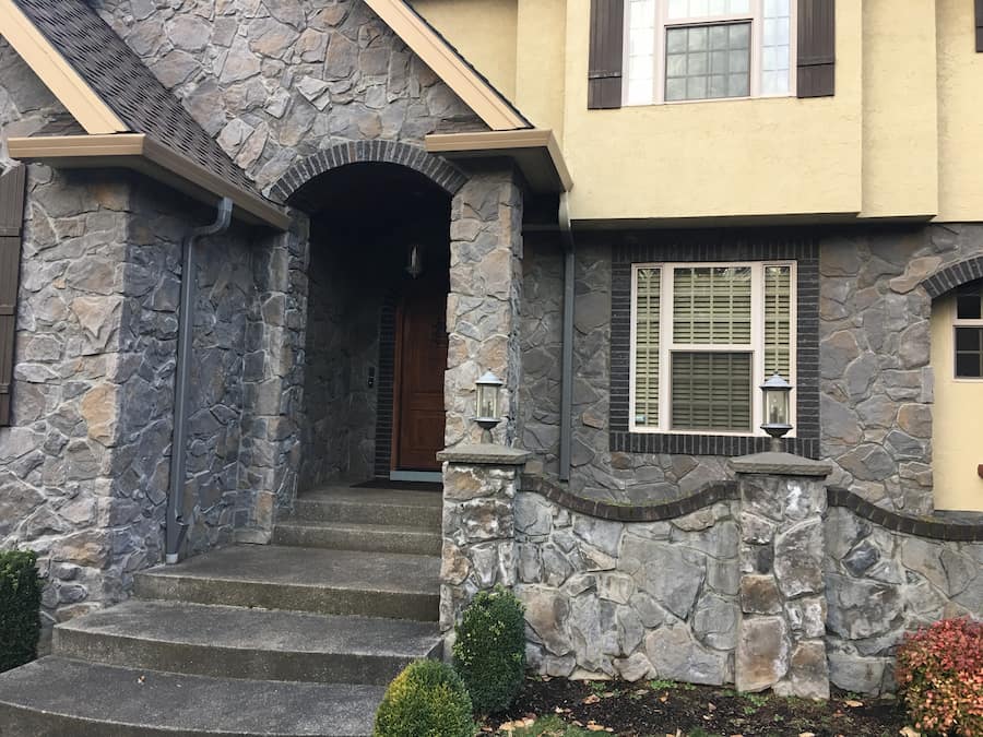 Fascia gutter and matching downspout installed beside a stone exterior